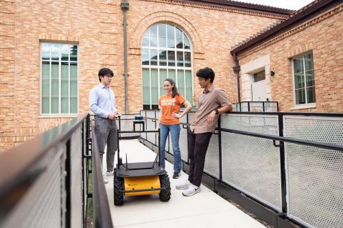 three students outside with robot